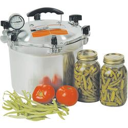 Pressure canner with some canned green beans next to it and some fresh tomatoes and green beans in front of it.