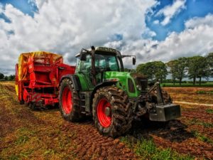 Green tractor pulling a piece of farm equipment across a field.