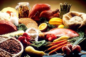 alt="a variety of healthy foods (proteins, vegetables, and grains) spread out on a table"