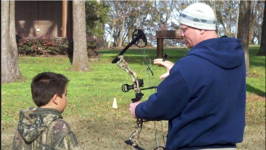 an adult volunteer coach showing a youth the parts of a compound bow