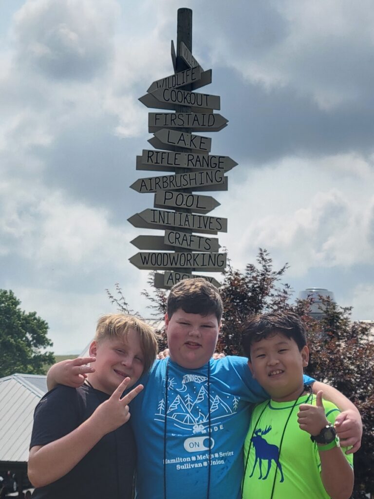 three boys next to a sign showing activities at camp