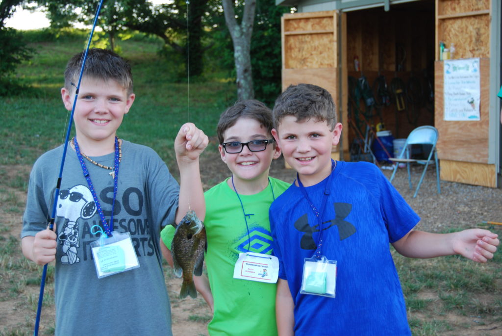 Three boys showing a fish that they caught at camp