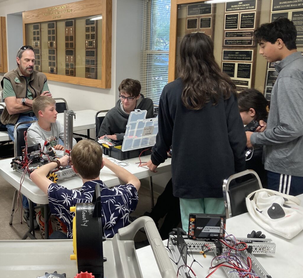 Students and a coach sitting at a table which contains a robot