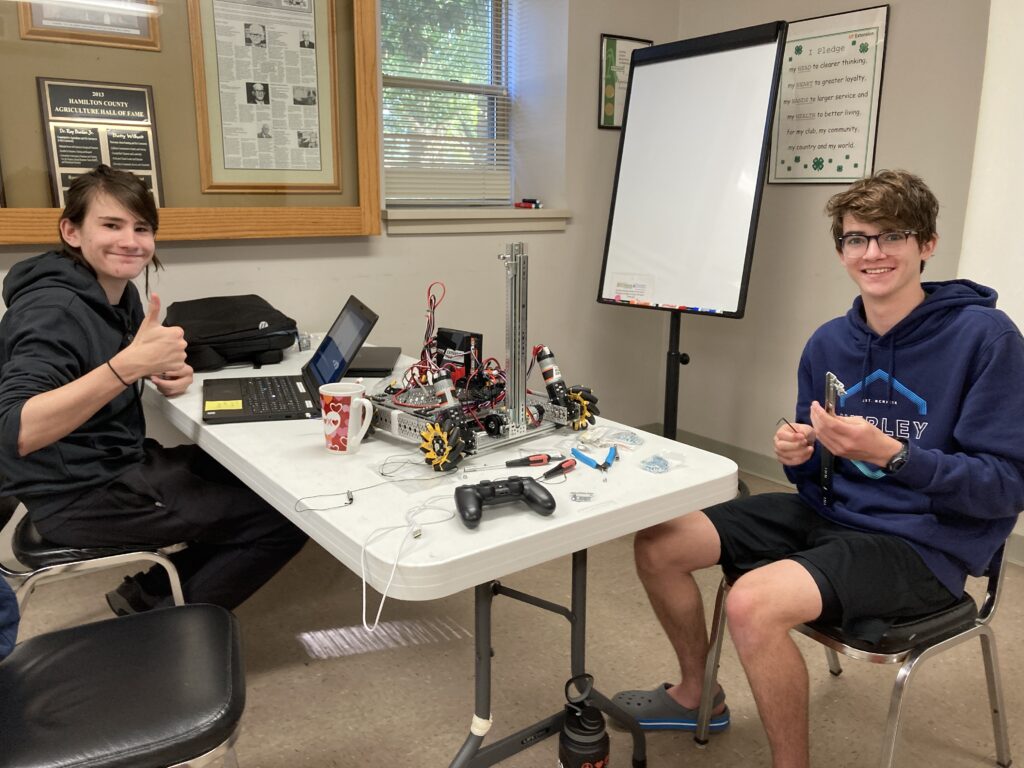 Two boys sitting at a table, working on a robot and a computer