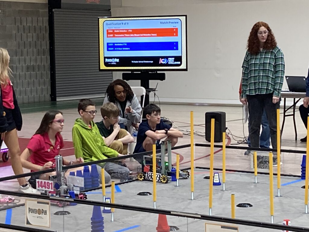 Coach and team members sitting next to a robot at a practice game