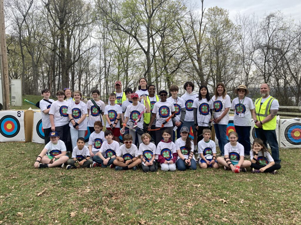 A group of children and club leaders pose in front of archery targets