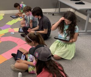 Children sit on the floor and work on iPads