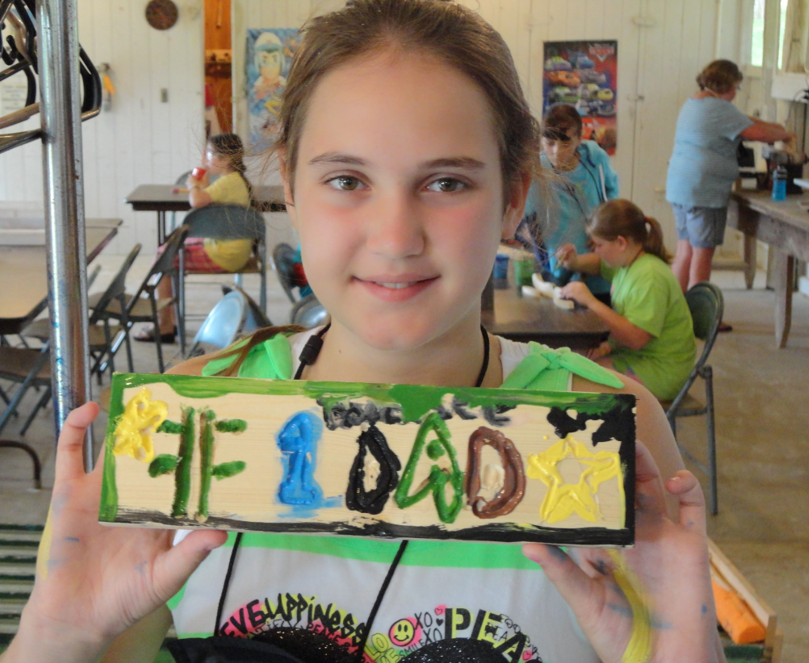 a girl holds up a plaque she made in woodworking