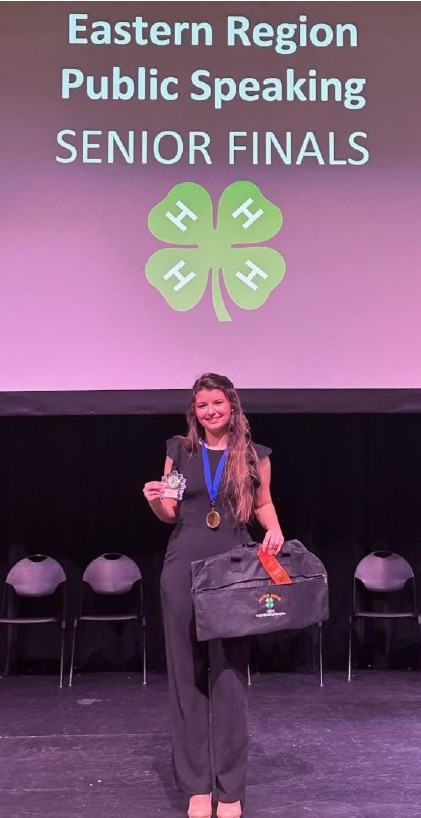A teen holds up a medal after winning a public speaking contest
